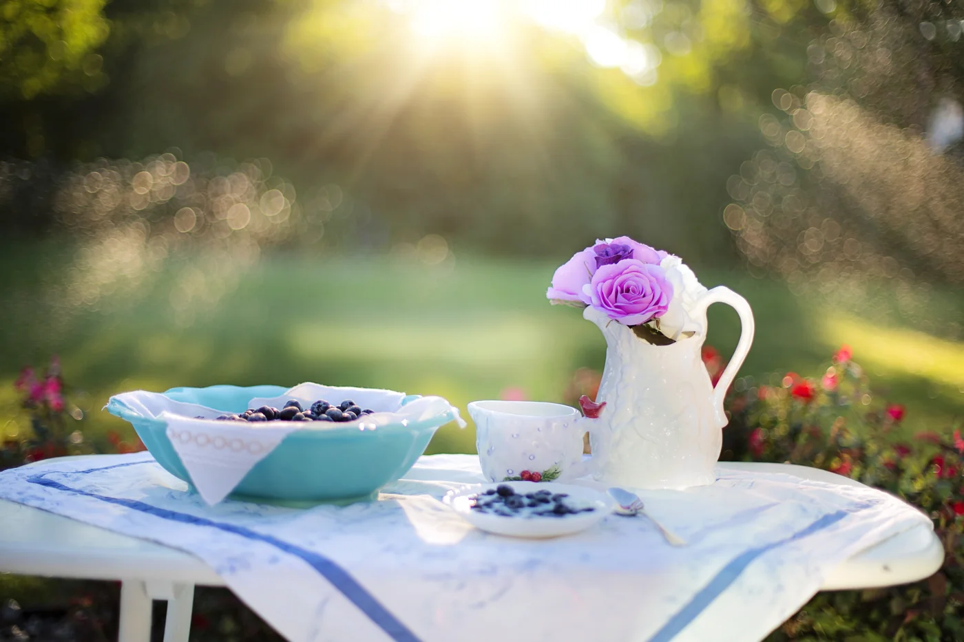 Table de petit-déjeuner dans un jardin, avec des myrtilles, une tasse et des fleurs