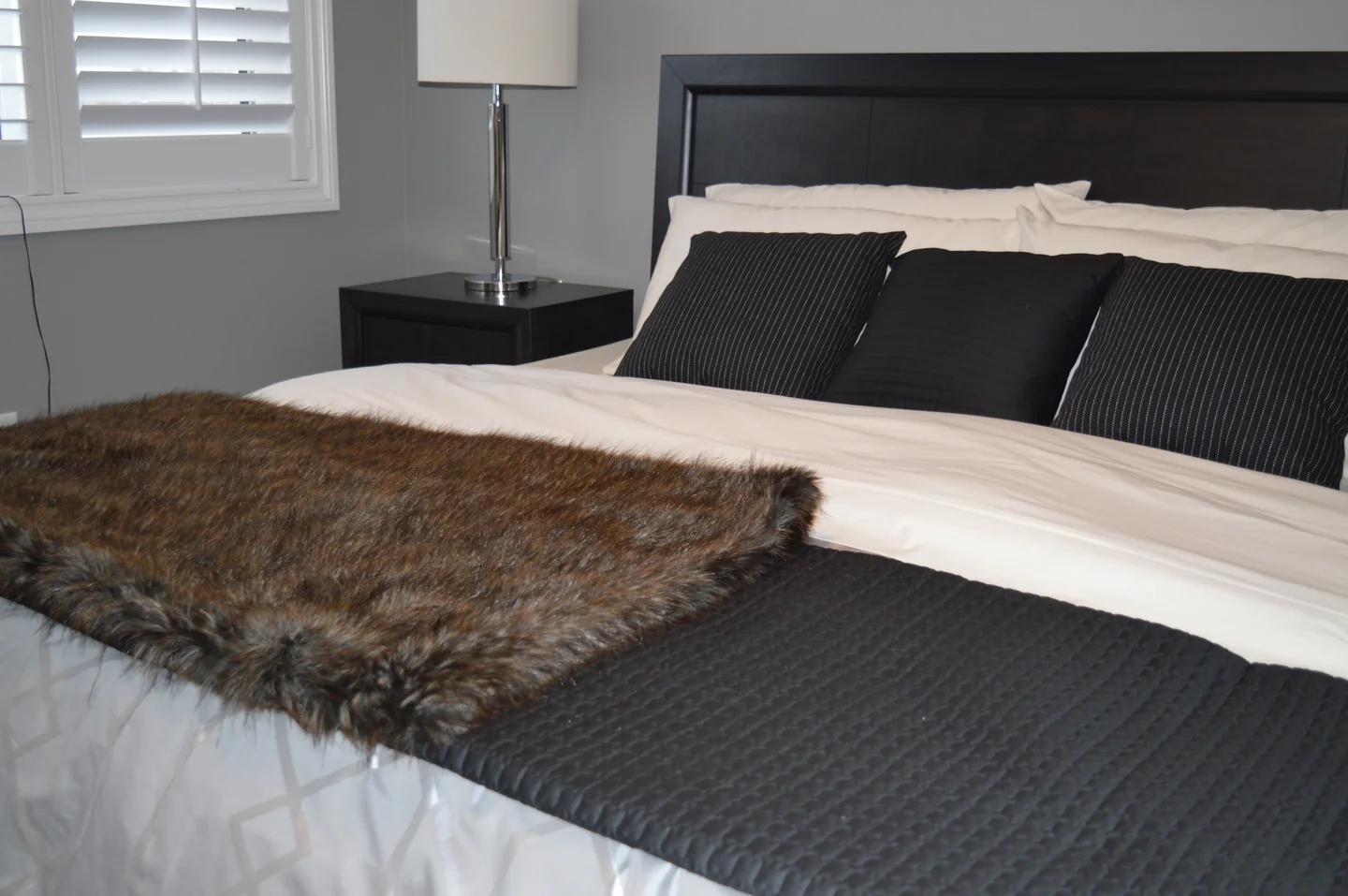 Illustration : chambre avec lit double, coussins foncés et linge blanc