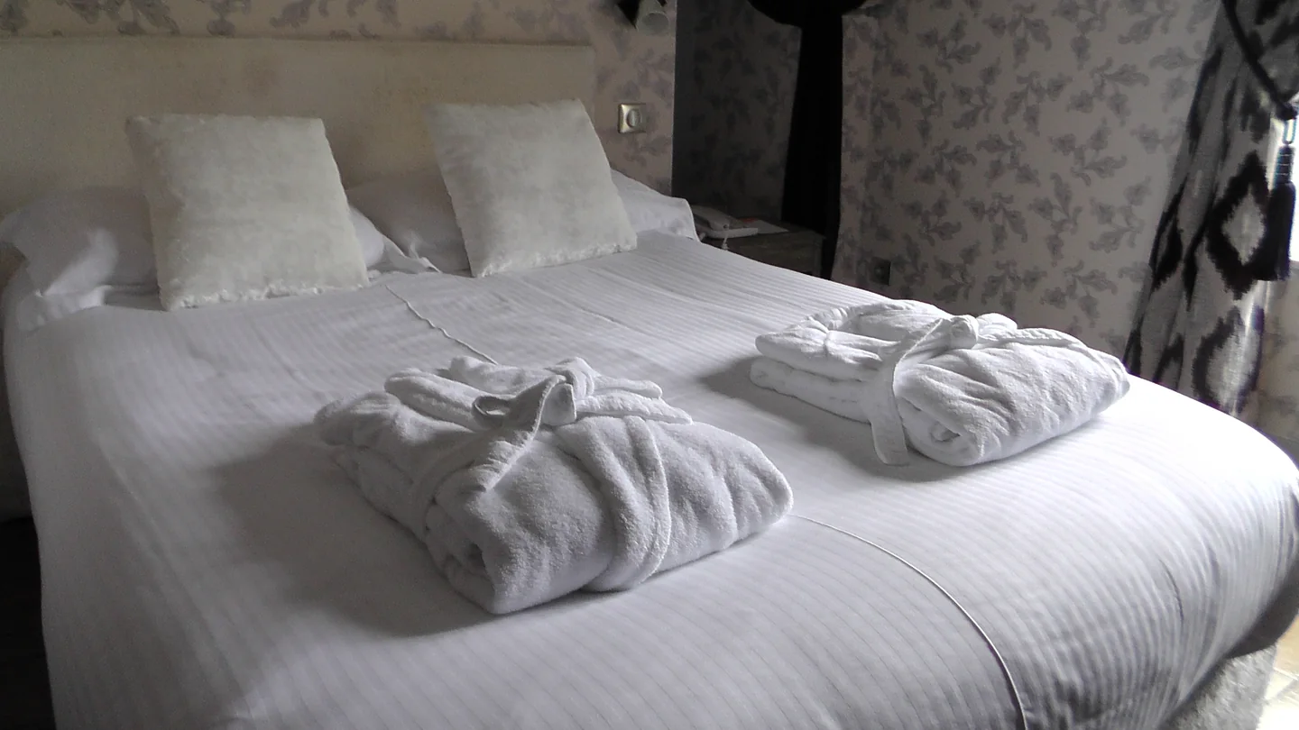 Illustration : lit avec linge blanc, serviettes pliées et peignoirs
